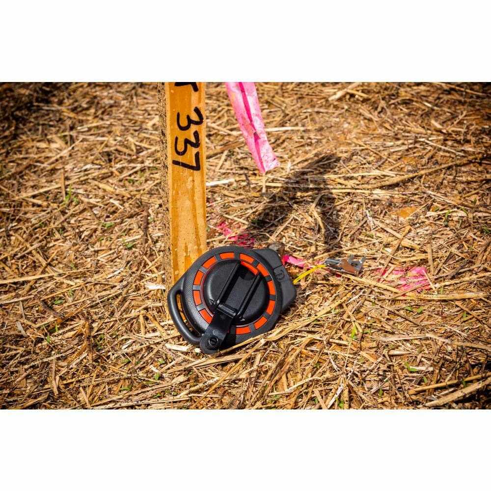 Crescent Lufkin ST100-07 100-foot steel tape measure resting on a construction site next to a marked lot stake, showcasing its rugged build for outdoor surveying and engineering environments.