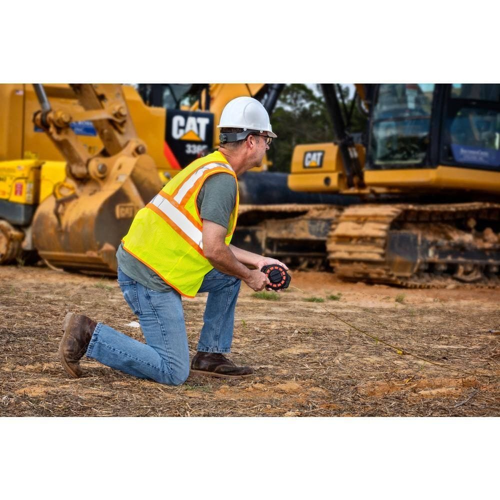 A contractor on a job site using the Crescent Lufkin 100-foot steel construction long tape to perform a long-distance layout measurement near heavy machinery.
