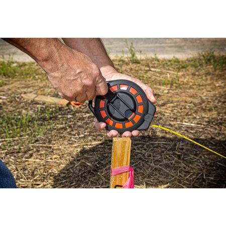An action photograph of a professional using the rapid rewind handle on the Crescent Lufkin 50-foot steel tape to retract the blade after taking a measurement at a residential construction site.