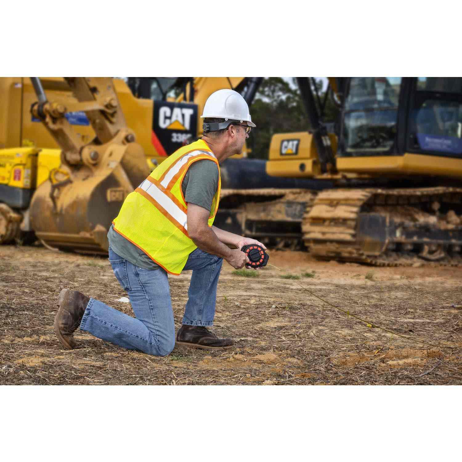 A lifestyle action photograph showing a surveyor in a safety vest using the Crescent Lufkin 50-foot steel tape measure to establish distances at a large-scale industrial construction site with heavy machinery.