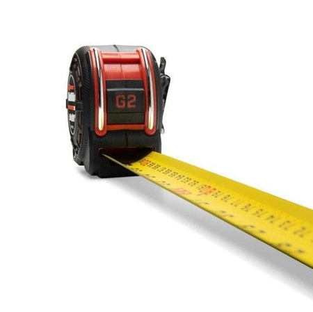 Perspective view looking down the extended 16-foot Shockforce G2 blade toward the case, highlighting the dual-sided yellow blade with high-contrast metric and SAE graduations and the industrial-grade 360-degree end hook.