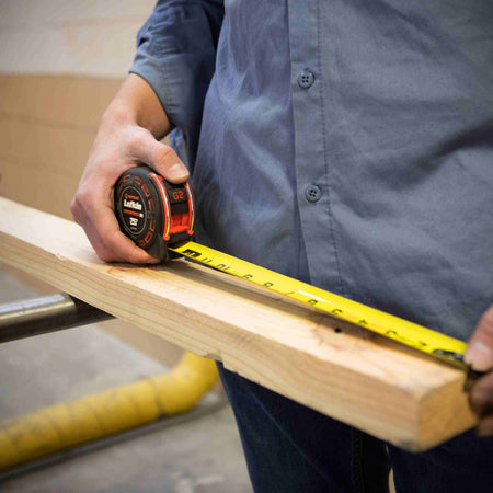 A professional tradesperson using the Crescent Lufkin Shockforce G2 tape measure to take a measurement on a piece of dimensional lumber, showcasing its compact ergonomics and high legibility.