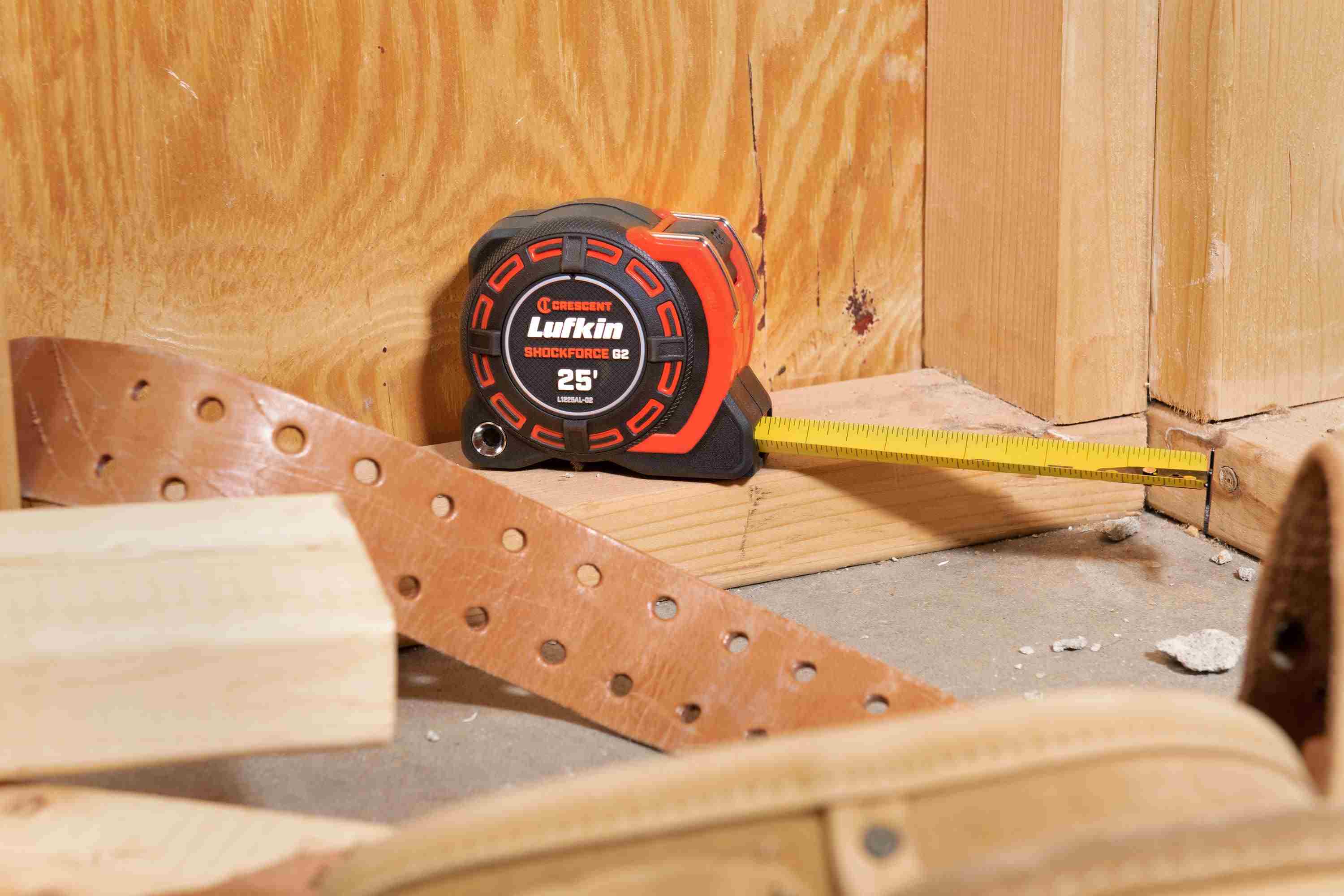 Close-up action shot of the 26-foot Shockforce G2 tape measure resting on a wooden stud, showing the blade's stability and the secure grasp of the diamond-coated end hook during industrial framing tasks.