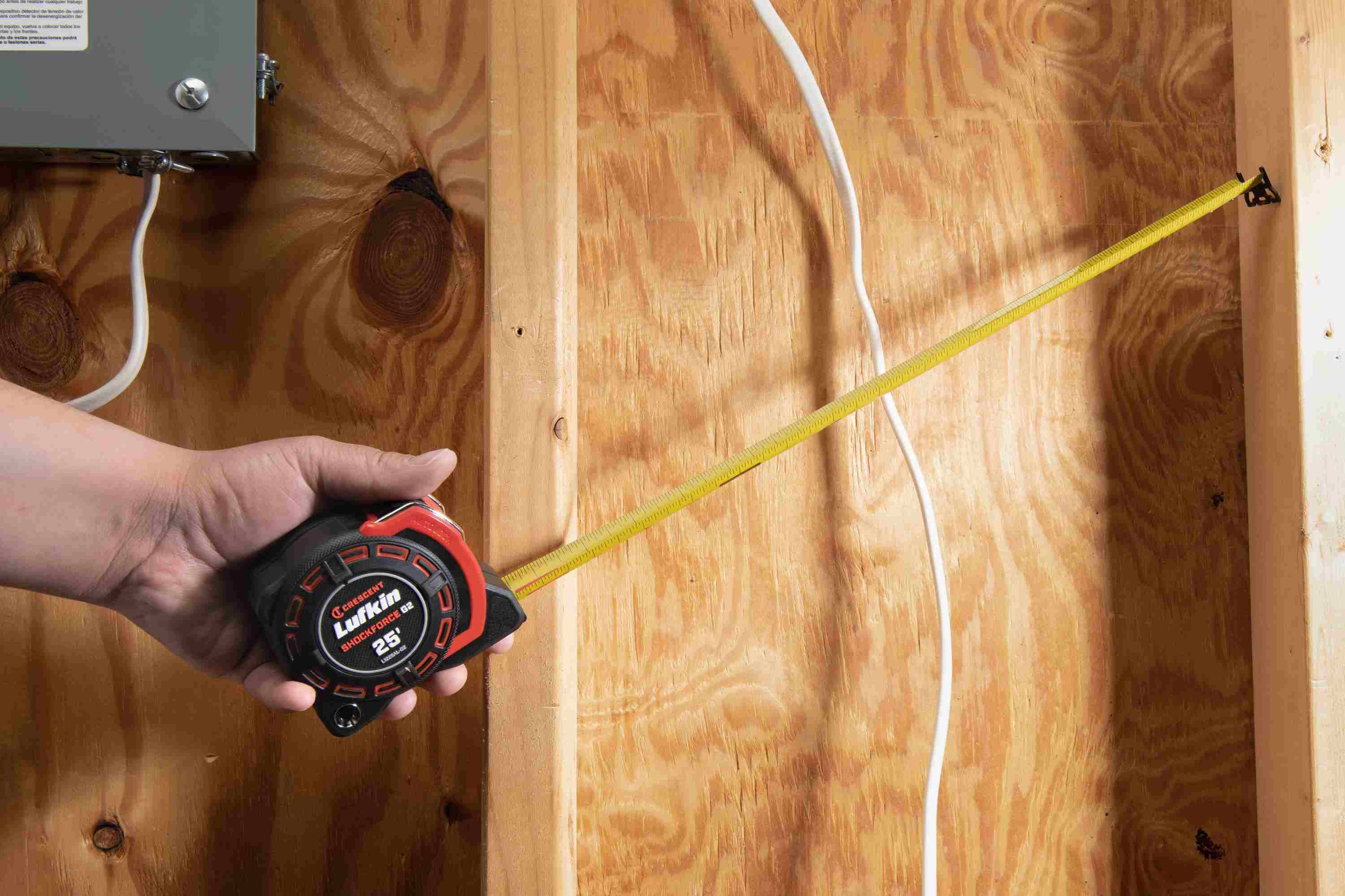 A tradesperson using the Crescent Lufkin Shockforce G2 auto-lock tape measure to measure a vertical distance on dimensional lumber within a wood-framed structure, demonstrating its high-legibility markings and ergonomic handling.