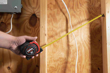 A tradesperson using the Crescent Lufkin Shockforce G2 auto-lock tape measure to measure a vertical distance on dimensional lumber within a wood-framed structure, demonstrating its high-legibility markings and ergonomic handling.
