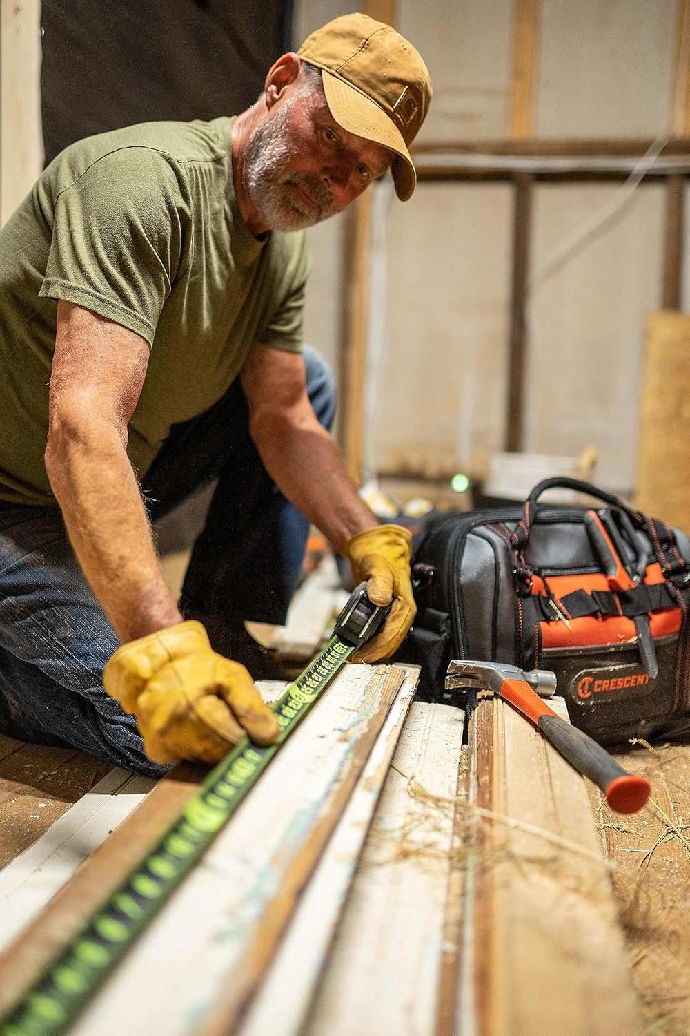 A contractor in a work environment using the Crescent Lufkin Shockforce Nite Eye 25-foot tape measure for layout work, with a professional tool bag and hammer visible in the foreground.