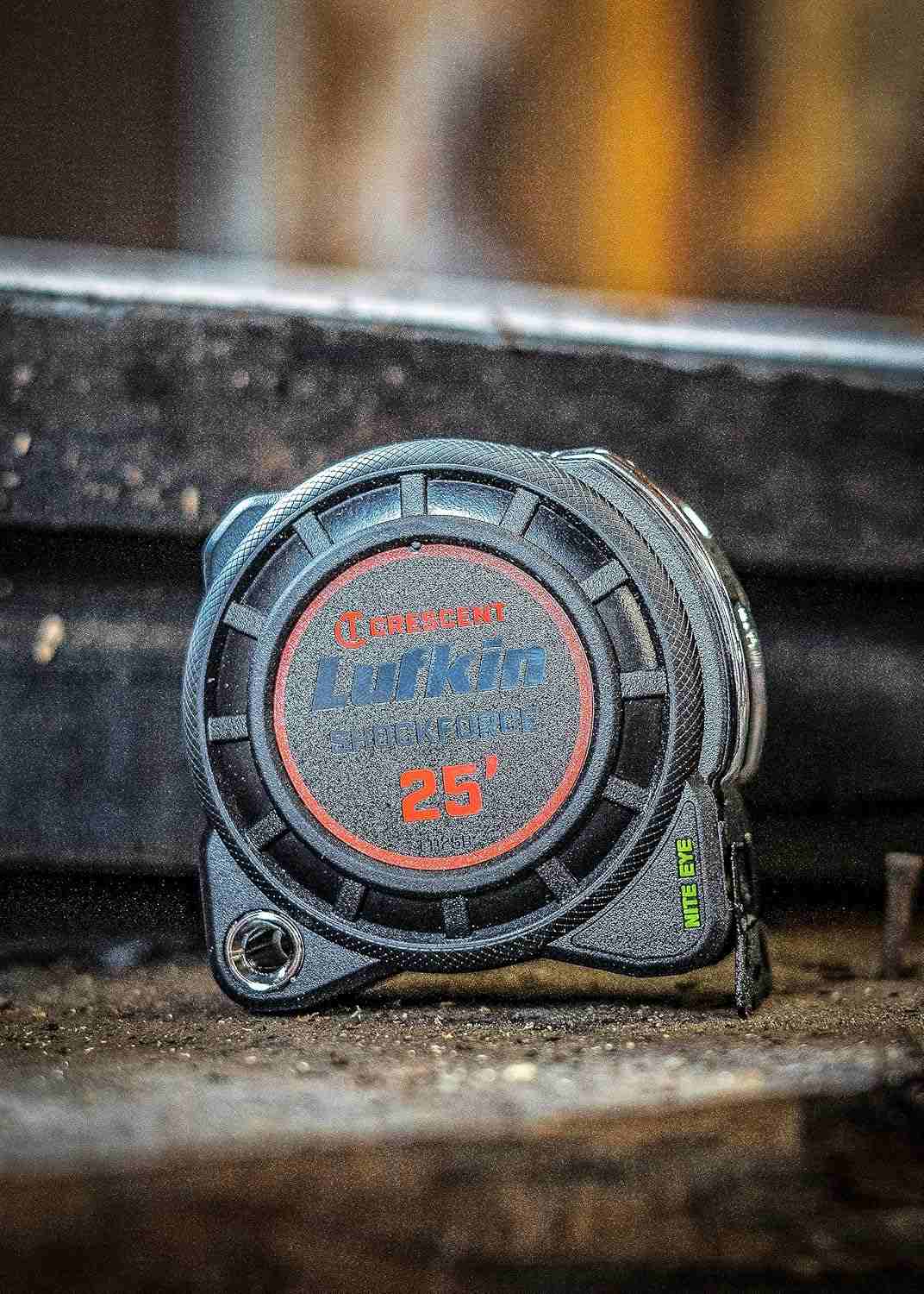 Close-up of the Crescent Lufkin Shockforce Nite Eye 25-foot tape measure case resting on a rugged, dark industrial surface, highlighting the durable impact-resistant housing and Nite Eye branding.