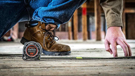 A tradesperson using the Crescent Lufkin Shockforce Nite Eye tape measure on a wooden floor at a construction site, demonstrating the tool's durability and professional job-site application.