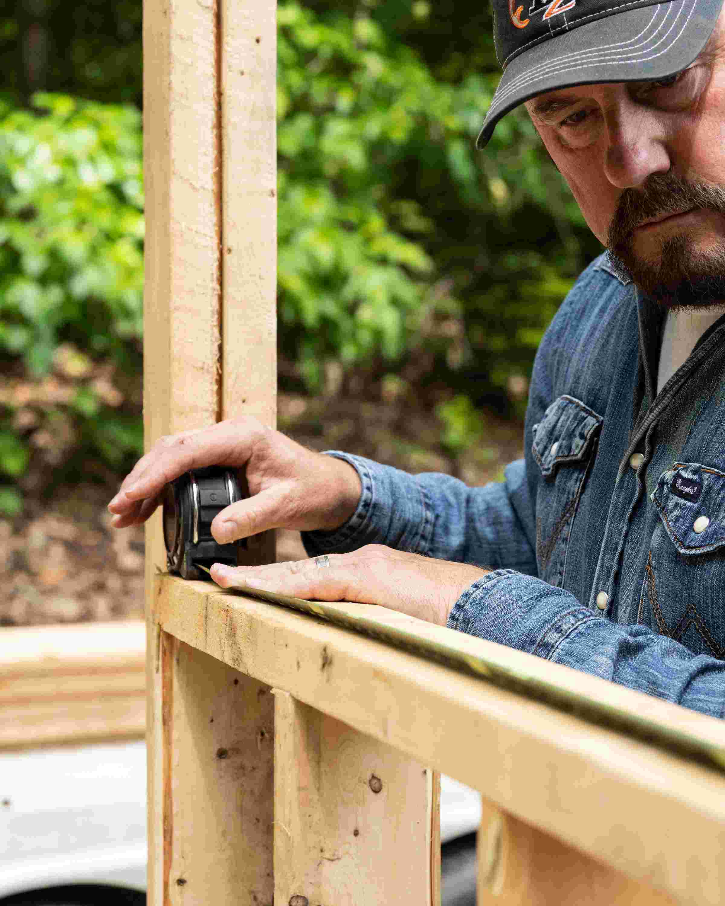 A professional contractor using the Crescent Lufkin Shockforce Nite Eye G2 tape measure to accurately measure and scribe a wooden wall stud on an outdoor construction site.