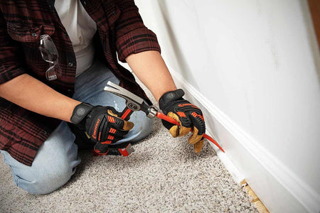 An action shot showing a person using the Crescent 8-inch molding pry bar to carefully lift and remove white floor molding from a wall during a home remodeling project.