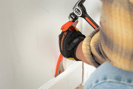 A close-up view of a worker using a hammer to strike the integrated striking surface of the Crescent molding bar to drive the precision ground edge behind a baseboard for removal.