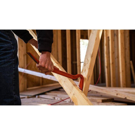 Construction worker using the curved end of the Crescent PB18 18-inch I-beam steel wrecking pry bar to aggressively pry apart wooden wall framing on a demolition site.