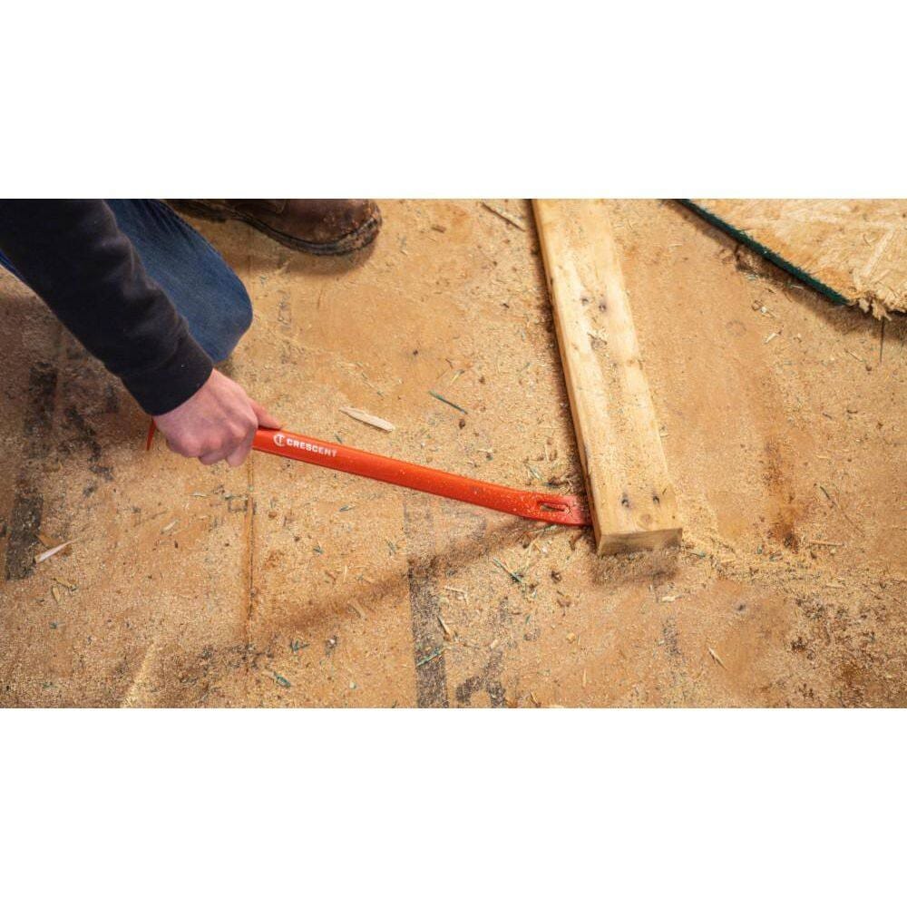 A worker using the straight edge of the Crescent demolition hand tool to wedge under and lift a piece of nailed lumber off a wood subfloor.