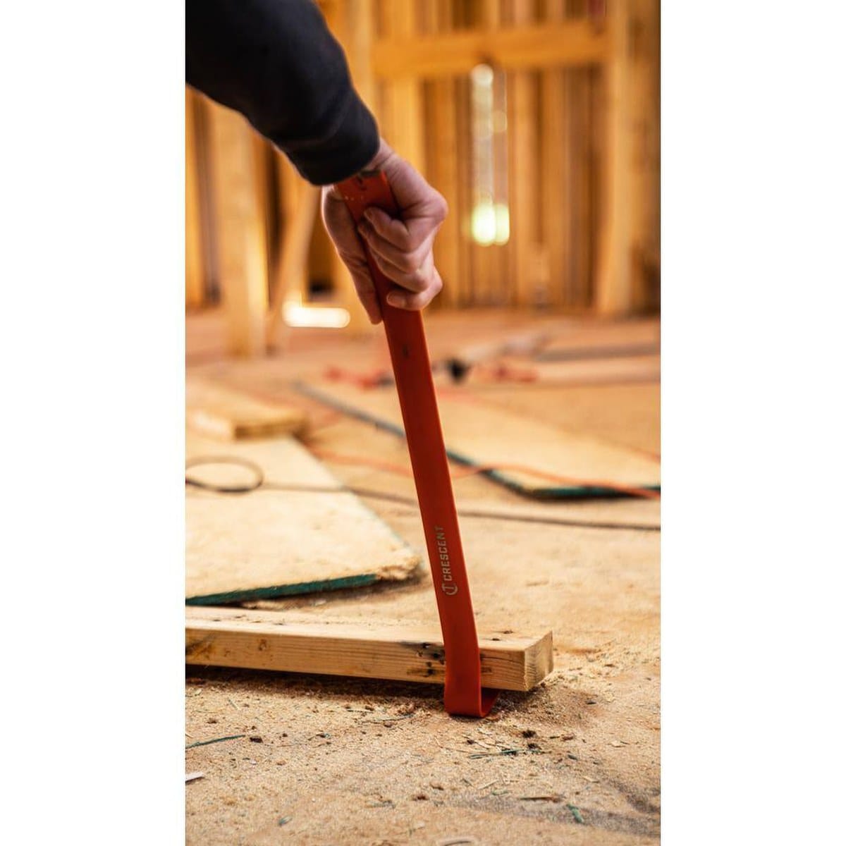 A worker using the Crescent 36-inch steel bar to pry a piece of lumber from a concrete floor, showcasing the tool's length and heavy-duty prying capability on a jobsite.