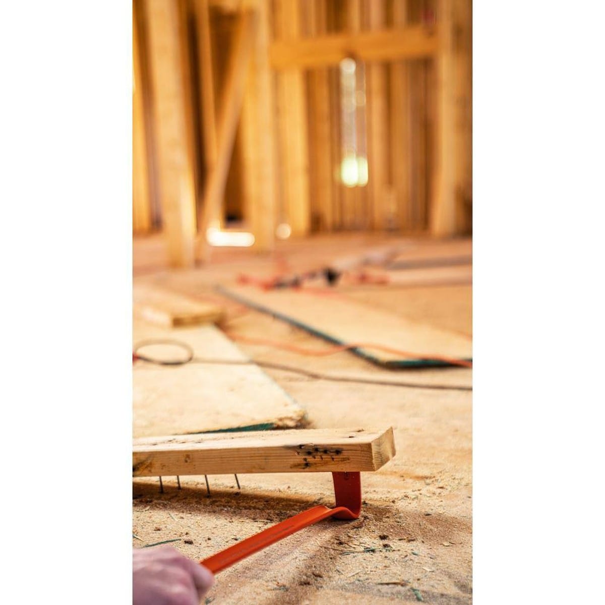 Action shot of a worker using the gooseneck end of the Crescent 36-inch wrecking bar to lift a wooden plank from a subfloor, highlighting the tool's ability to extract multiple nails simultaneously with its high-leverage design.