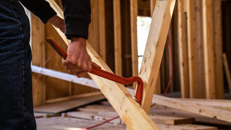 Action shot of a worker using the Crescent steel wrecking bar to pry apart heavy wooden framing members, demonstrating the tool's strength and leverage in a construction setting.