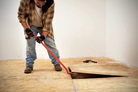A worker using the 36-inch Crescent I-beam wrecking bar to lift a heavy plywood subfloor panel, illustrating the 40% lighter design that helps reduce user fatigue during demolition.