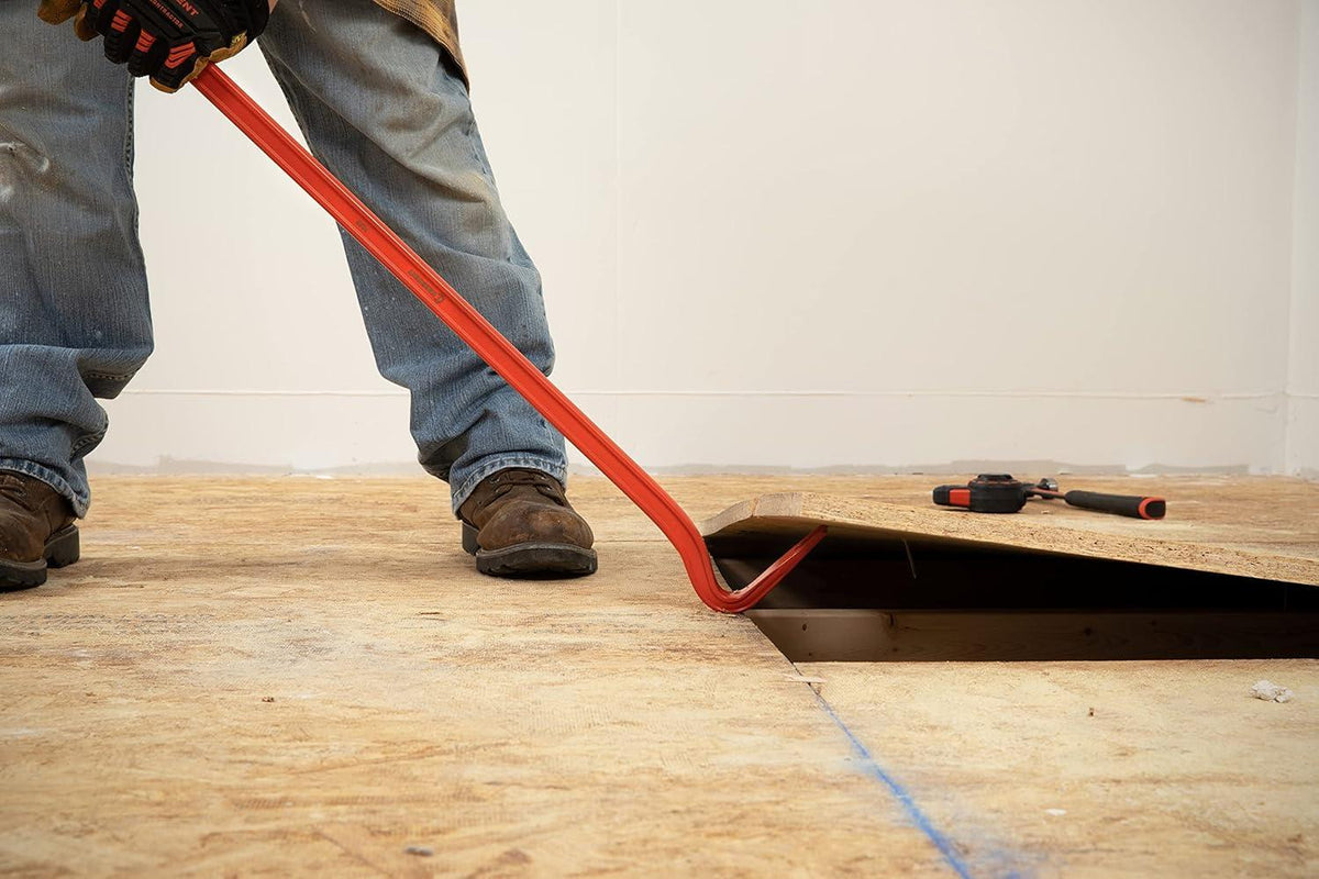 Close-up action view of the gooseneck end of the Crescent PB36 pry bar being used to lift a wooden floor board, highlighting the tool's ability to bite into tight gaps.
