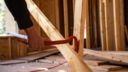 Side action view of the gooseneck end of the 42-inch bar biting into a wooden floor plate, highlighting the tool's ability to provide massive leverage in tight gaps.