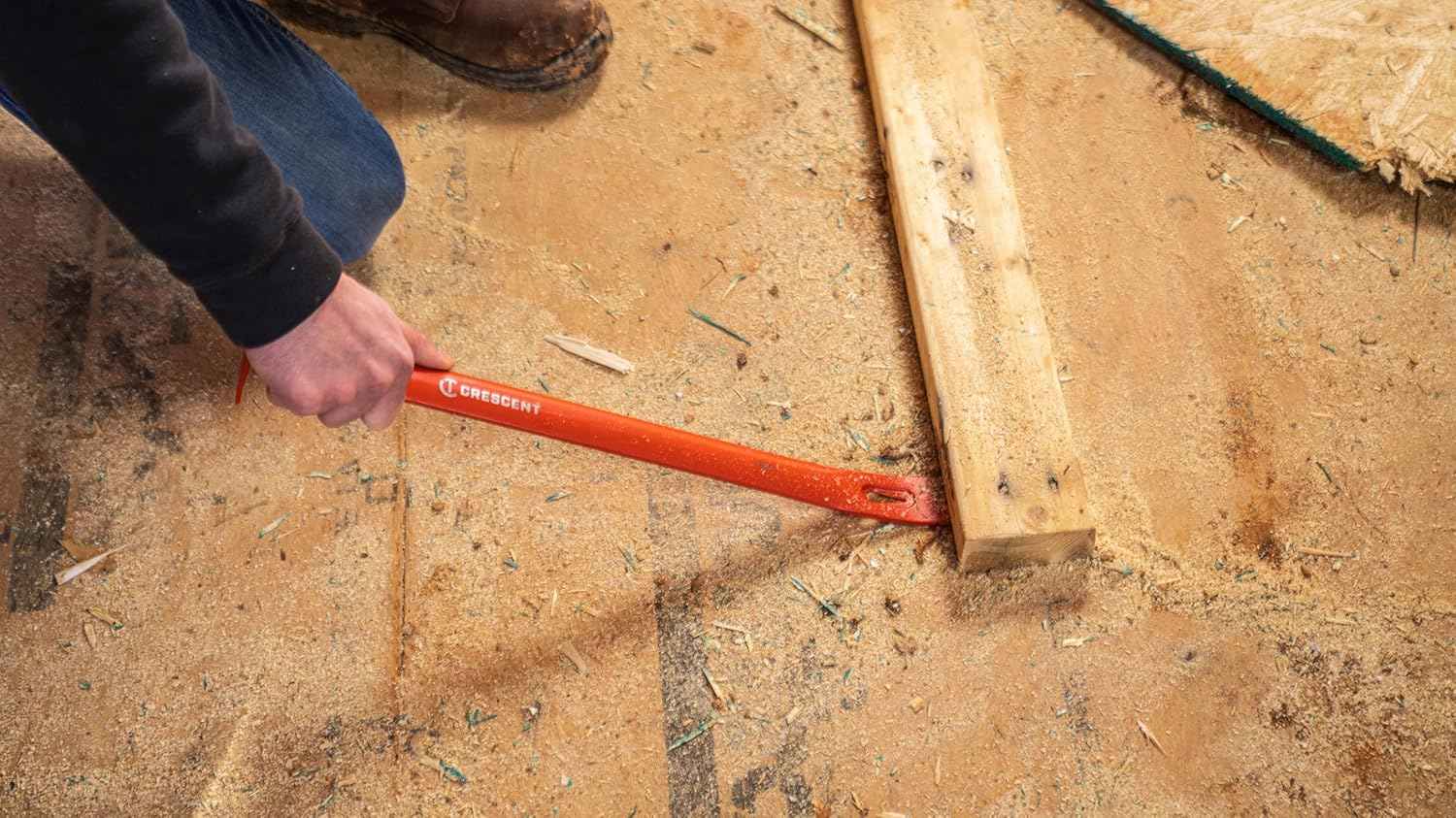 A worker using the Crescent PB42 steel bar to pry up a floor board from a concrete subfloor, showcasing the tool's heavy-duty demolition capability.