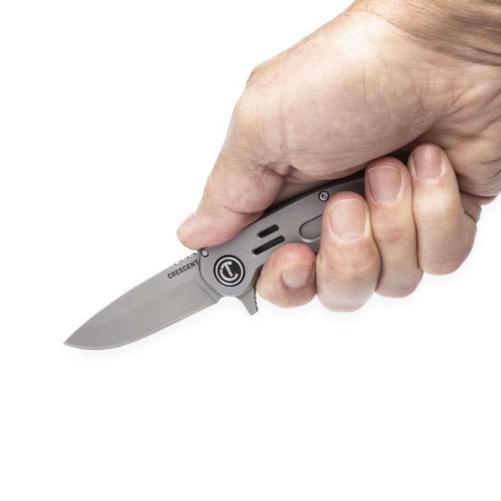 An overhead close-up shot of a hand gripping the opened Crescent pocket utility knife, illustrating the hand-and-finger contact points designed for maximum grip and ergonomic cut control.