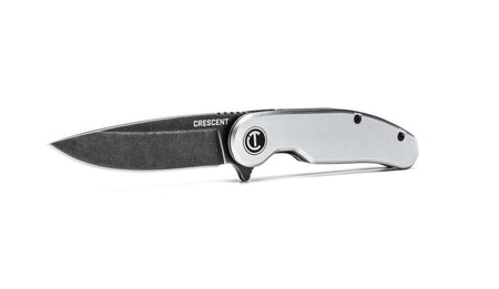 An alternate low-angle studio shot of the fully deployed Crescent folding pocket knife resting on its aluminum frame edge, highlighting the sleek profile of the fine-edge drop point blade and the manual flipper tab mechanism near the pivot.