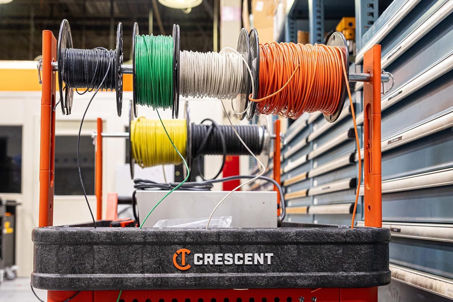 A functional demonstration of the electrician's wire spool holder in a workshop setting, showing several colored wire reels mounted on the cart's corner posts for easy pulling and organization.