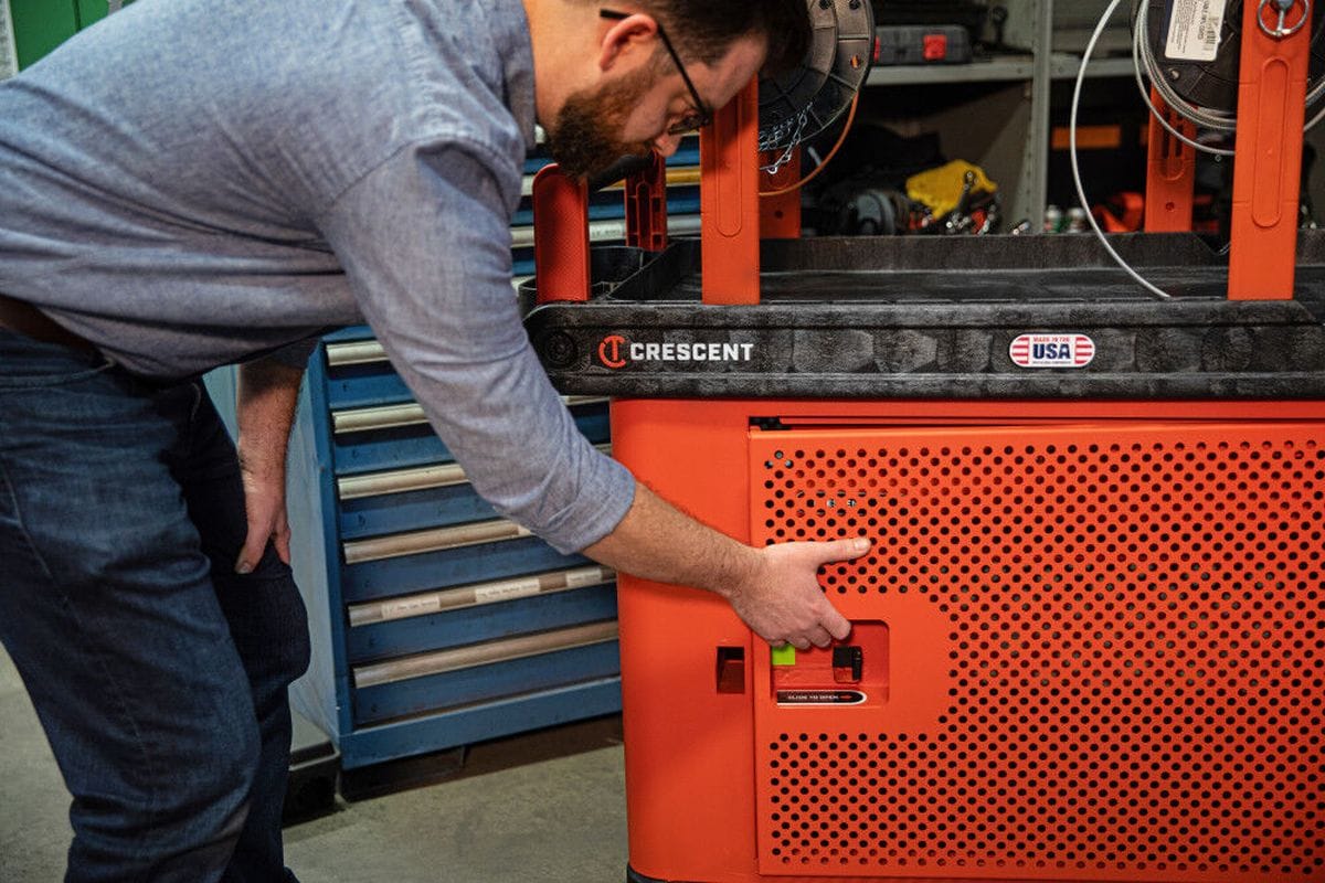 A functional demonstration showing a worker kneeling to unlock the single-door mesh security panel, highlighting the high-visibility inventory monitoring and secure storage capabilities of the Crescent cart.