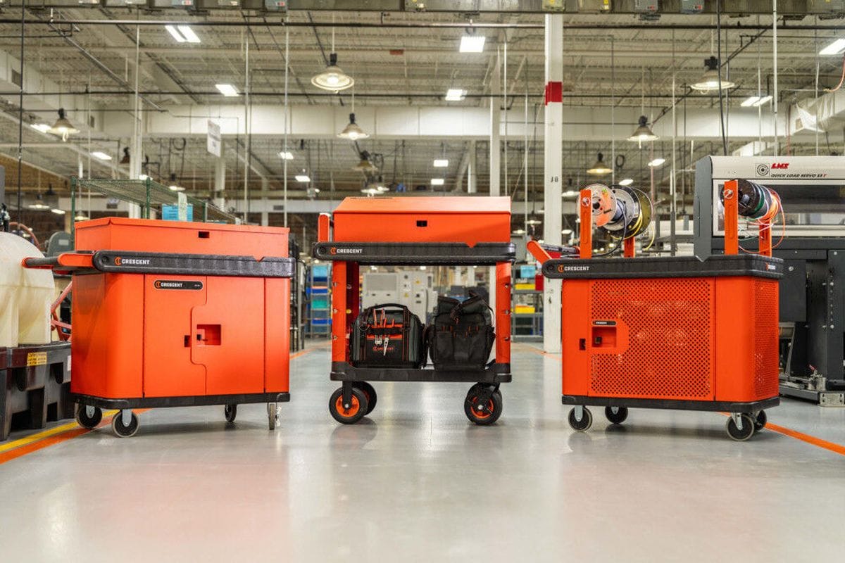 A wide-angle warehouse shot displaying three Crescent RAILWORKS modular carts in different configurations, including fully enclosed mesh security models and open-shelf carts holding professional tool bags and wire reels.
