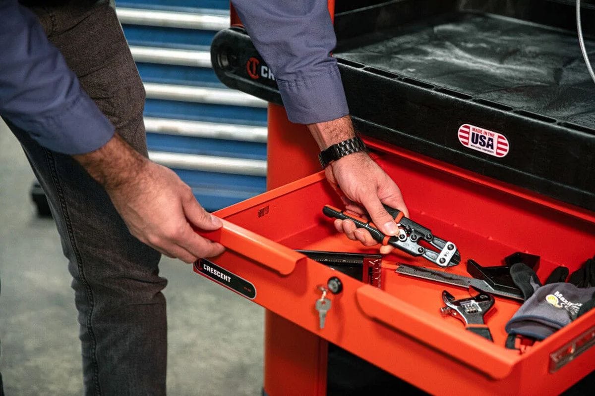 A functional demonstration of the industrial sliding drawer in use, showing a professional tradesman reaching for hand tools and precision instruments stored securely within the key-locked rawhide orange drawer.