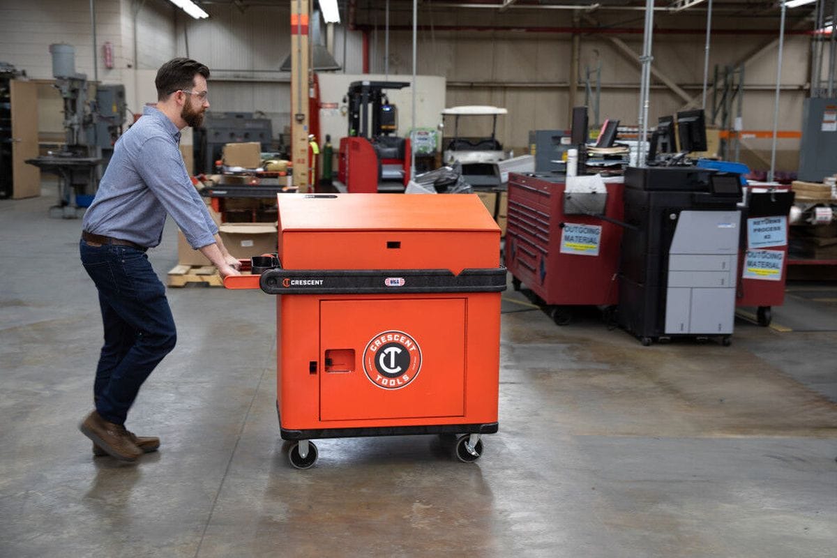 An application shot showing a professional worker in a warehouse setting pushing the orange Crescent RAILWORKS utility cart, demonstrating its smooth maneuverability and ergonomic 3-position adjustable comfort grip handle.