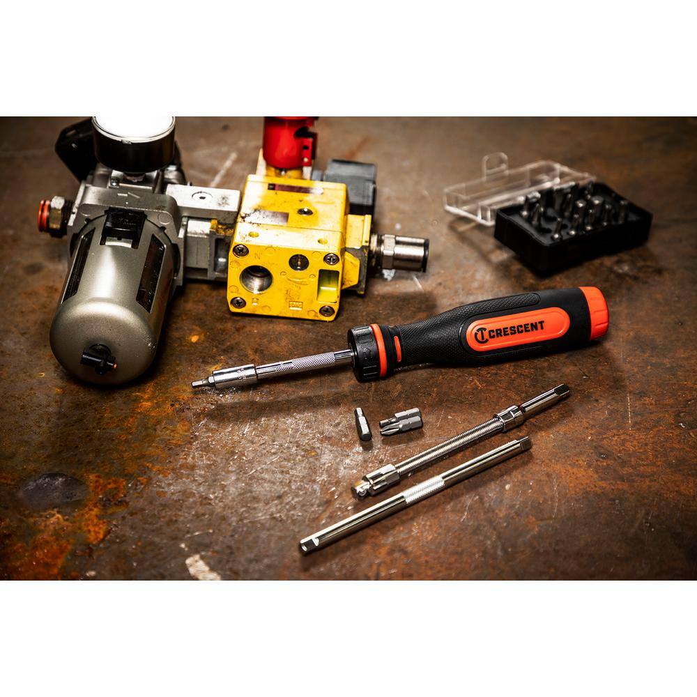 Workplace application view of the Crescent ratcheting bit screwdriver set sitting on a weathered metal workbench layout next to industrial pneumatic regulator assemblies and modular extension rods.