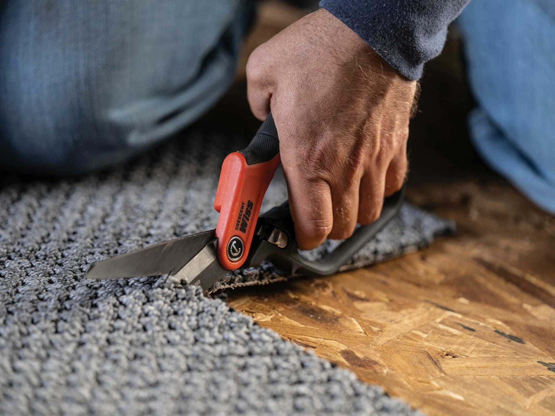 A close-up action shot of a person's hand using the Crescent Wiss CW11TM tradesman shears to cut through a piece of thick gray carpet.