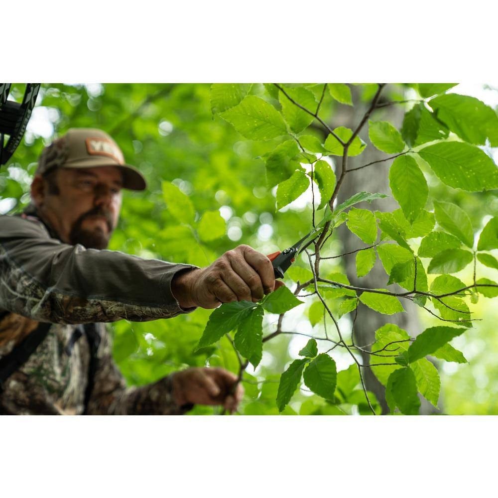An action photo of a tradesman using the Crescent Wiss titanium coated shears to precisely trim small branches in a wooded environment, demonstrating the tool's portability and sharp cutting power.