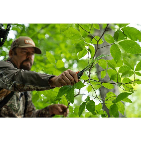 An action photo of a tradesman using the Crescent Wiss titanium coated shears to precisely trim small branches in a wooded environment, demonstrating the tool's portability and sharp cutting power.