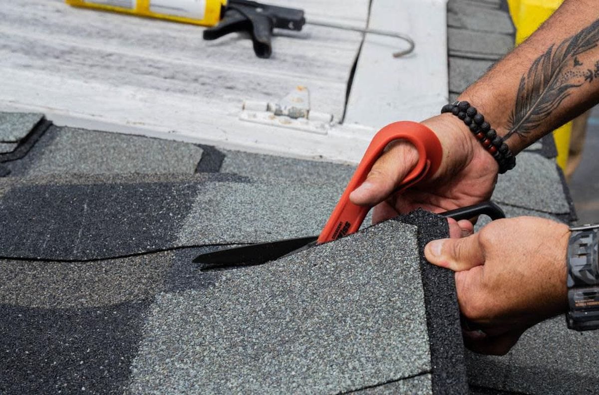 A roofing professional using the Crescent Wiss CW10T shears to cut through thick composite shingles, demonstrating the tool's power and effectiveness in outdoor construction environments.