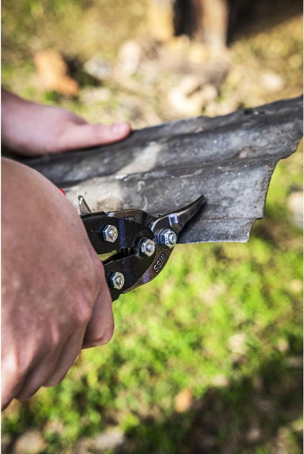 Close-up application photo showing the Crescent Wiss snips making a precise curved cut in corrugated metal, demonstrating the elite material control provided by the serrated cast blades.