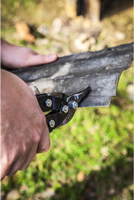 Close-up application photo showing the Crescent Wiss snips making a precise curved cut in corrugated metal, demonstrating the elite material control provided by the serrated cast blades.