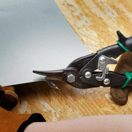 A tradesman wearing leather work gloves using the Crescent Wiss M2P compound action aviation snips to smoothly perform a right-curved cut on a piece of sheet metal.