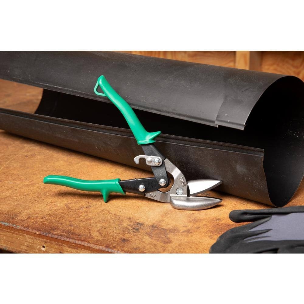 An industrial metal worker uses the Crescent Wiss M7R MetalMaster snips to perform a precise right-arc cut on a metal pipe, showcasing the tool's maneuverability and the integrated single-handed latch operation.