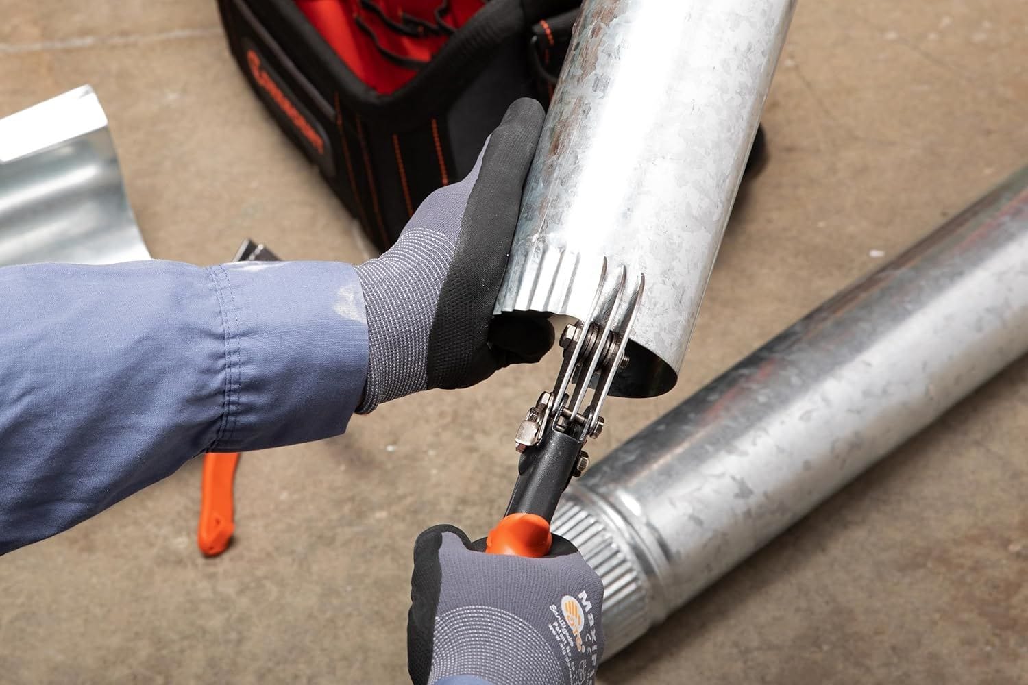 An action photograph of a professional technician using the Crescent Wiss WC5SN crimper to create a male fitting end on a round galvanized metal pipe in an HVAC installation setting.