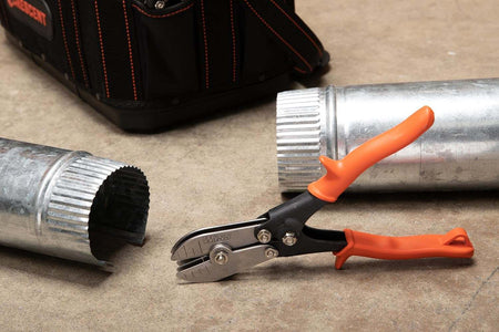A lifestyle action photograph showing the Crescent Wiss 5-blade HVAC pipe crimper resting next to a finished crimped slip-joint connection on a galvanized sheet metal duct, showcasing professional jobsite results.