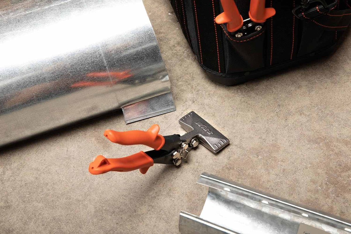 A lifestyle photograph showing the Crescent Wiss WS4N offset seamer resting on a concrete floor next to galvanized sheet metal ducting and a professional tool bag, highlighting its use in HVAC installations.