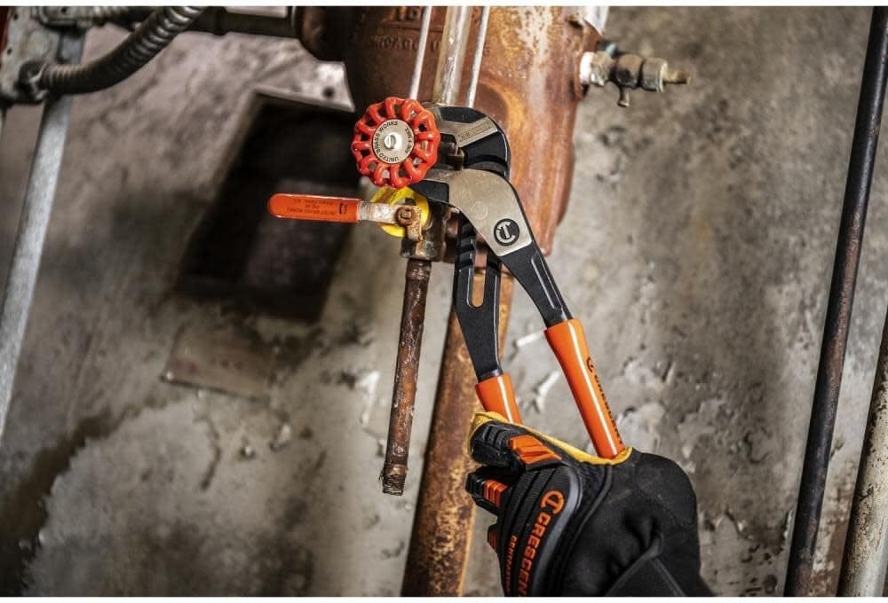 An action shot of a professional tradesman using the Crescent RTZ212 12-inch pliers to grip and turn a metal pipe valve in a tight, industrial setting.
