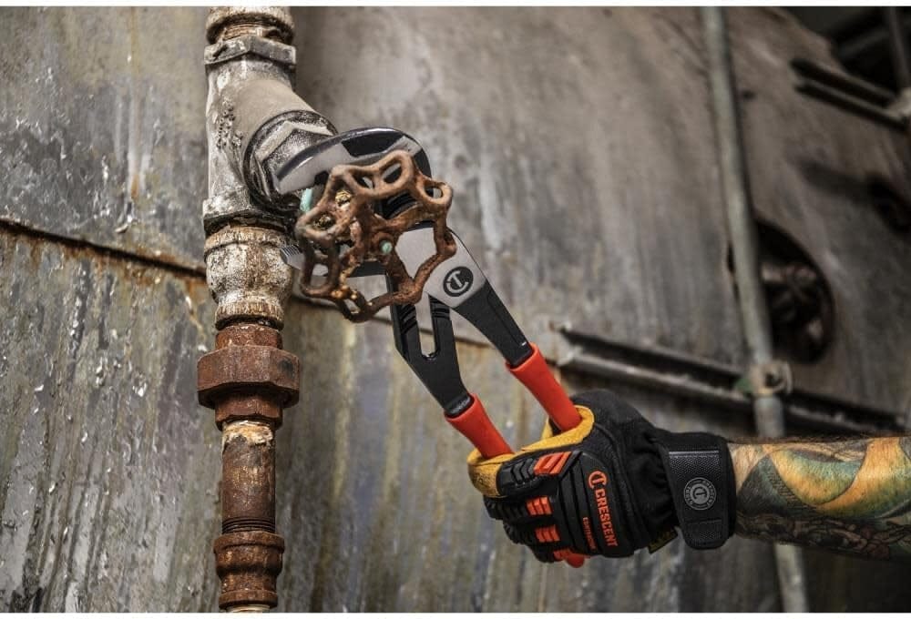 Close-up action shot of a worker using the Crescent 12-inch Z2 water pump pliers to tighten a large metal pipe fitting on an industrial site.