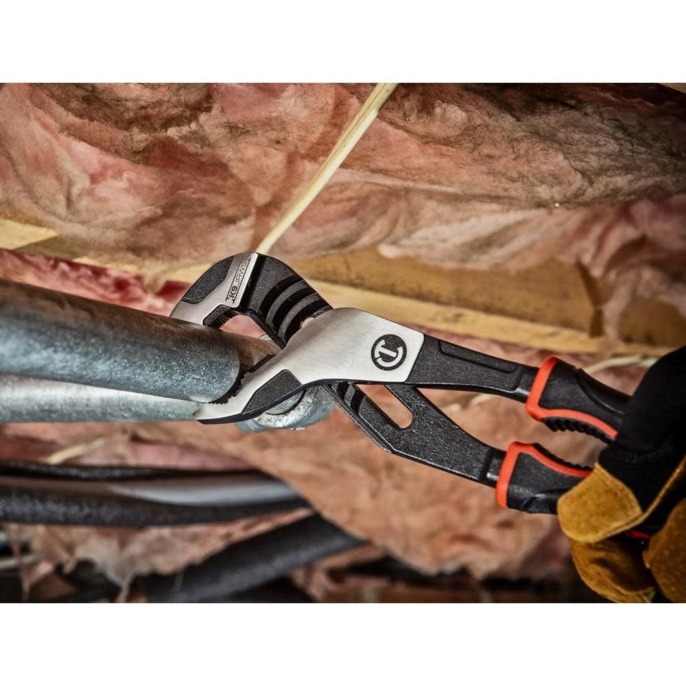 Close-up action shot of the Crescent Z2 pliers gripping a metal pipe in a confined ceiling space with pink insulation in the background.