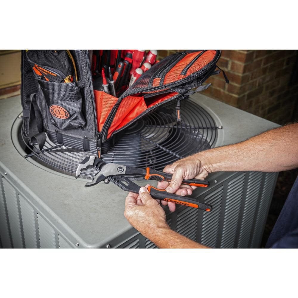 Lifestyle image showing a user holding the Crescent Z2 pliers in front of an HVAC unit and an open tool bag filled with other tools.