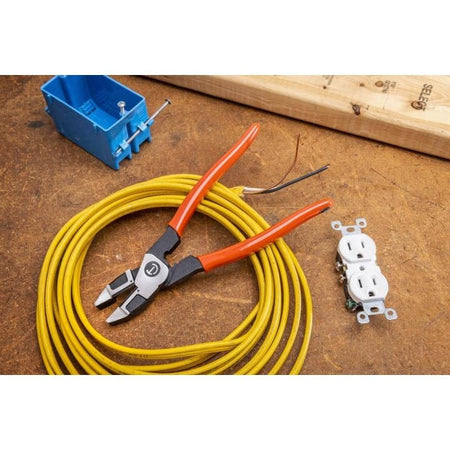 Electrical tools arranged on a workbench, featuring red-handled wire cutters placed on coiled yellow wire, a white duplex outlet, stripped black and white wires, and a blue electrical box. The setup illustrates components used in residential wiring projects.