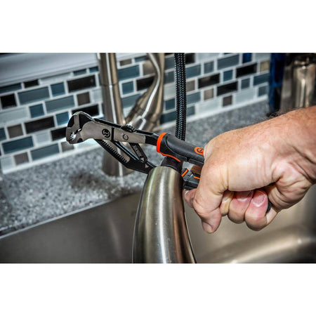 A detailed close-up lifestyle shot of a technician using the one-handed automatic adjusting pliers to grip and steady a curved chrome bathroom plumbing fixture above a steel sink.