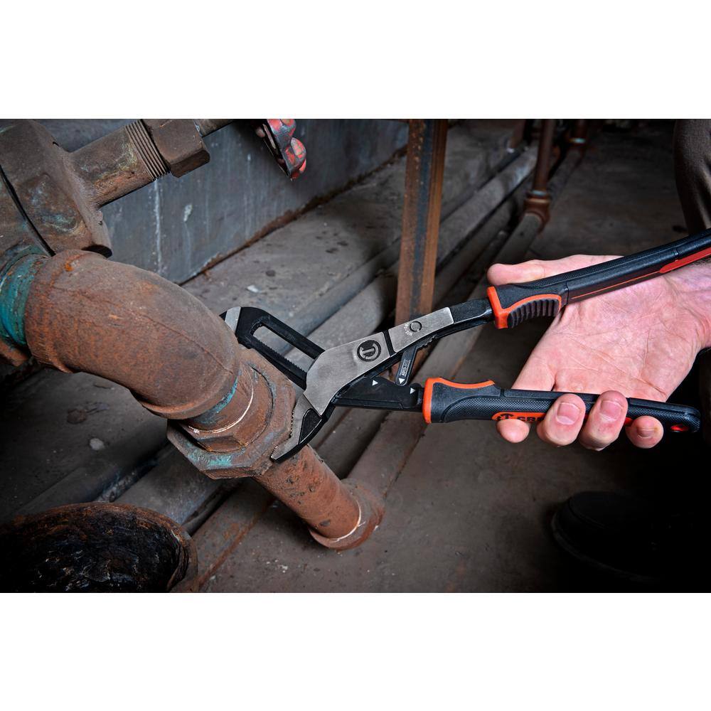 An industrial facility maintenance photo showing a plumber using the drop-forged alloy steel jaws of the Crescent 6-inch tongue and groove pliers to grip and turn a heavily rusted iron pipe coupling in a crawlspace.